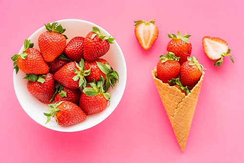 Top view of natural strawberries in bowl and waffle cone on pink surface