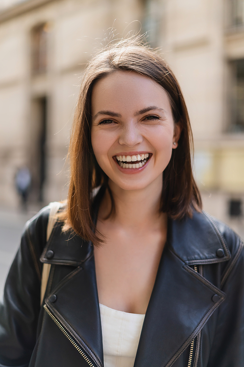 portrait of positive young woman in leather jacket laughing while