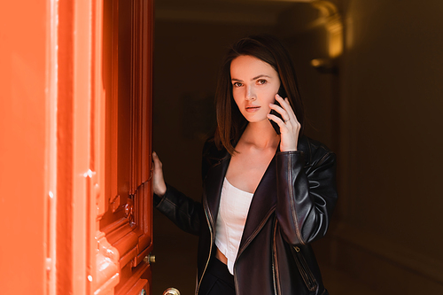 young woman in black leather jacket talking on smartphone near orange door