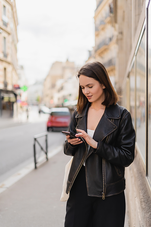 young woman in black leather jacket messaging on smartphone on street in paris