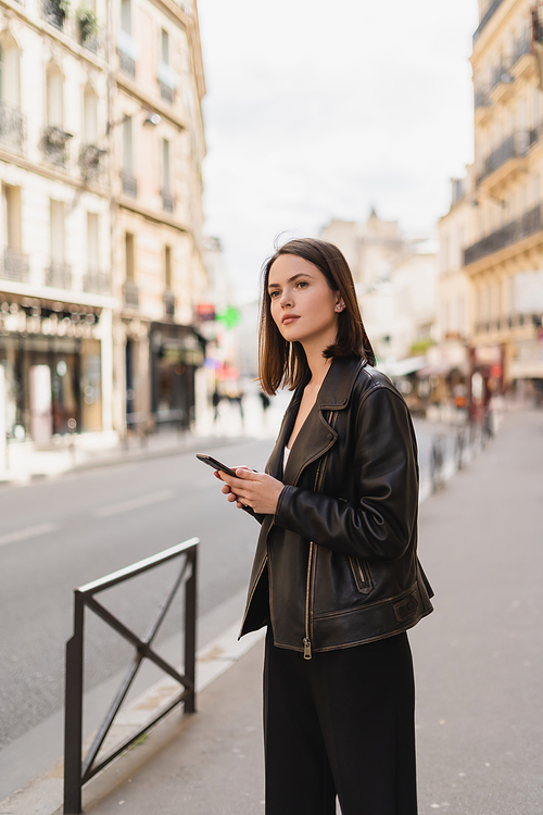 young woman in black leather jacket holding smartphone on street in paris