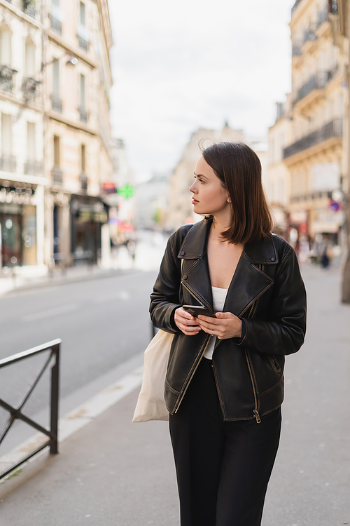 young woman in black jacket holding smartphone on street in paris