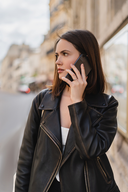 portrait of young woman in stylish jacket talking on smartphone on street in paris