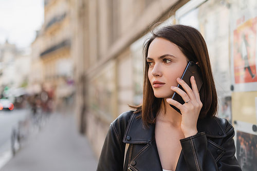 portrait of brunette young woman in stylish jacket talking on smartphone on street in paris