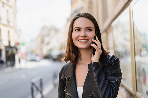 smiling young woman in stylish jacket talking on smartphone on street in paris