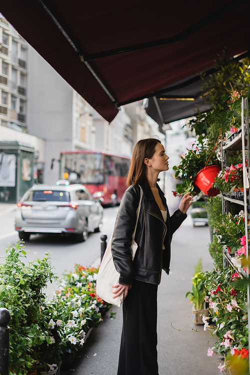 side view of woman with canvas shopper bag looking at green potted plants on street in paris