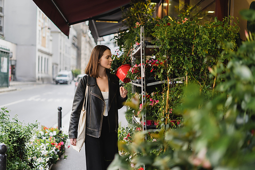 stylish young woman with canvas shopper bag looking at green potted plants on street in paris