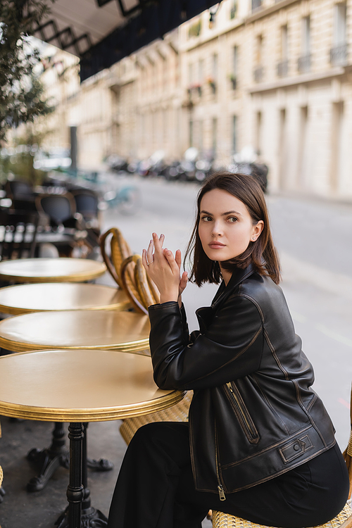 stylish young woman in black leather jacket sitting in french cafe on summer terrace
