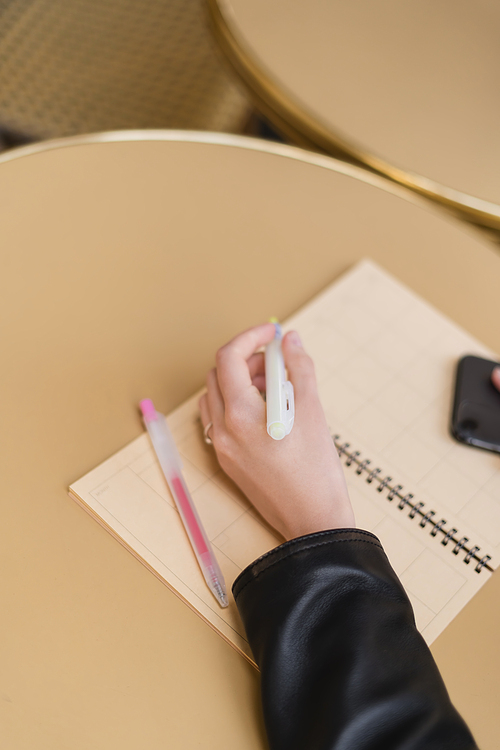 cropped view of woman holding marker pen near blank notebook on round table