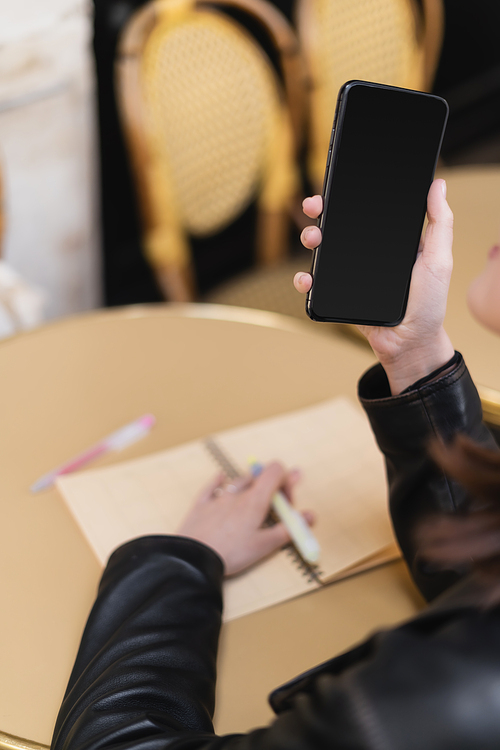 cropped view of woman holding smartphone with blank screen near blurred notebook on round table