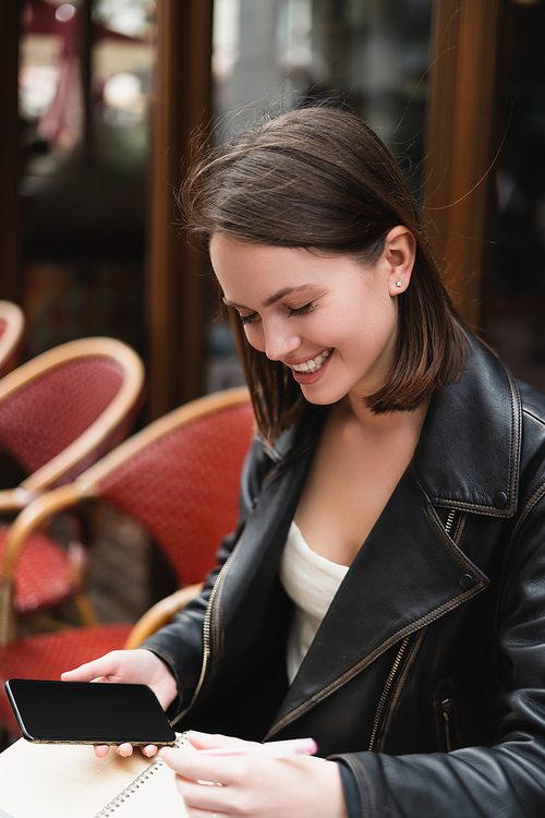 portrait of smiling woman holding smartphone with blank screen in outdoor cafe