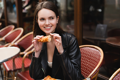 cheerful woman holding freshly baked croissant in outdoor cafe in paris