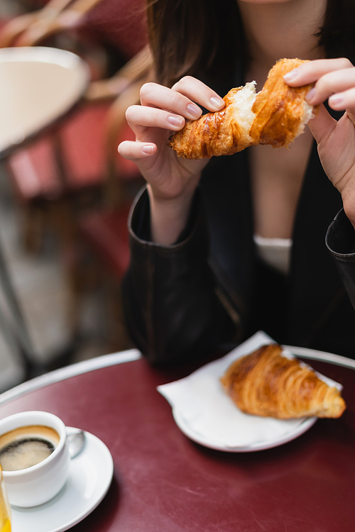 cropped view of woman holding croissant near cup of coffee in outdoor cafe in paris