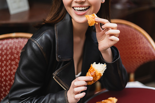 partial view of happy woman holding fresh croissant in outdoor cafe in paris