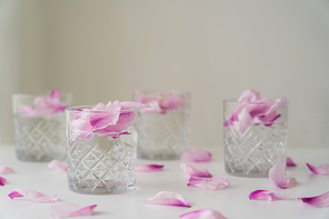 crystal glasses with tonic and petals on white surface and blurred grey background