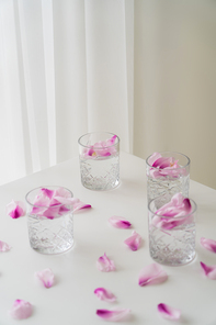 high angle view of glasses with tonic and floral petals on white tabletop and grey background