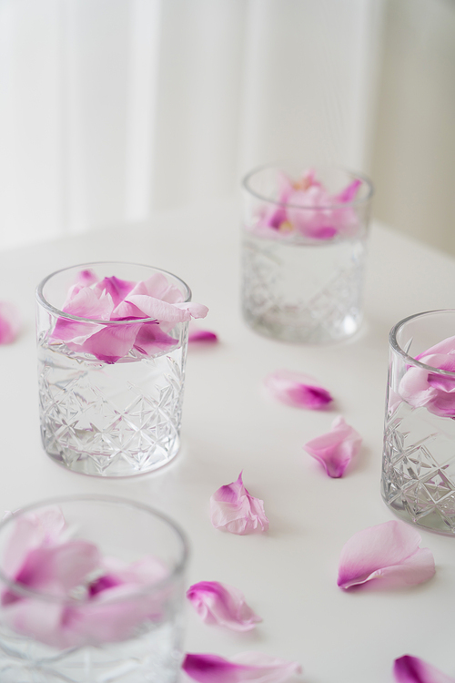 crystal glasses with tonic and natural floral petals on white tabletop and blurred background