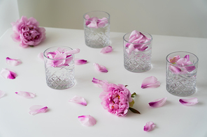 glasses with tonic and floral petals near pink peonies on white tabletop and grey background