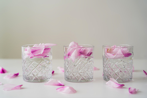 crystal glasses with floral petals and tonic on white tabletop isolated on grey