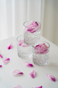crystal glasses with tonic and floral petals on white tabletop and grey background