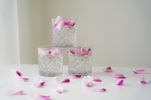 crystal glasses with tonic and floral petals on white surface and grey background
