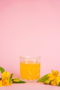glass of fresh citrus juice and yellow tropical flowers on pink background