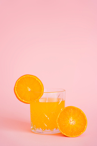 glass of refreshing juice and sliced orange on pink background