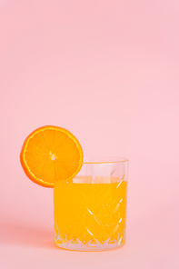 glass of pure citrus juice with slice of fresh orange on pink background
