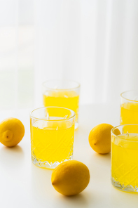 glasses with natural lemonade near whole lemons on white and blurred background