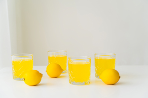 whole lemons near glasses with pure citrus juice on grey background with copy space