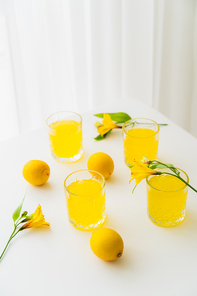 glasses with lemonade near fresh lemons and yellow alstroemeria flowers on white tabletop