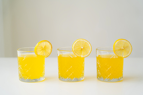 slices of fresh lemon on glasses with natural citrus juice on white surface isolated on grey