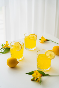 glasses of lemonade with slices of juicy lemon near alstroemerias on white tabletop