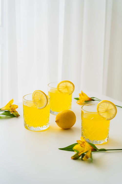 fresh citrus tonic near lemons and yellow alstroemeria flowers on white background