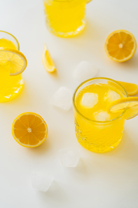 high angle view of glasses with iced citrus tonic and cut lemons on white surface