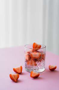 transparent glass of tonic water with cut strawberries on grey background