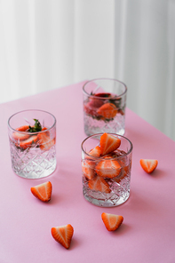 faceted glasses of tonic water with fresh chopped strawberries on white tabletop
