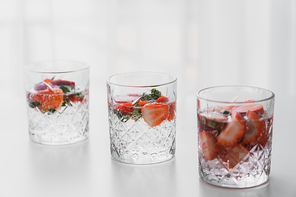transparent glasses of tonic drink with chopped strawberries on white surface
