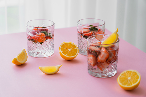 fresh tonic water with chopped strawberries near cut lemons on white tabletop