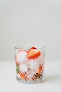 glass with iced tonic water with chopped strawberries on white surface isolated on grey