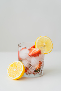 iced tonic drink with chopped strawberries and juicy lemon on white surface isolated on grey
