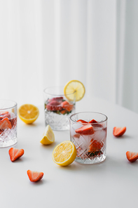 glasses with iced strawberry tonic near cut lemons on white tabletop