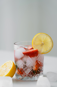 cold tonic with fresh strawberries and lemon slice on white surface isolated on grey