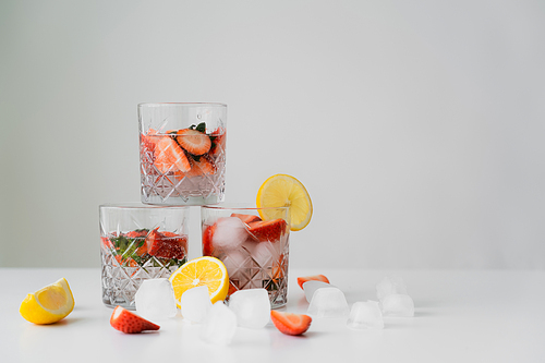 refreshing tonic drink with strawberries near cut lemons and ice cubes isolated on grey