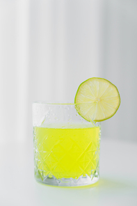 faceted glass with natural lemonade and slice of lime on grey background