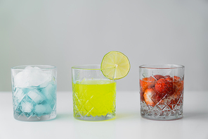 lemonade and strawberry tonic near glass with ice cubes on white surface isolated on grey