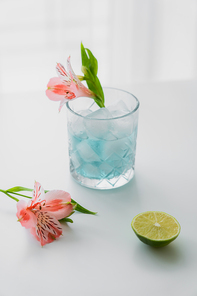 glass with iced tonic water near pink alstroemeria flowers and lime on white surface