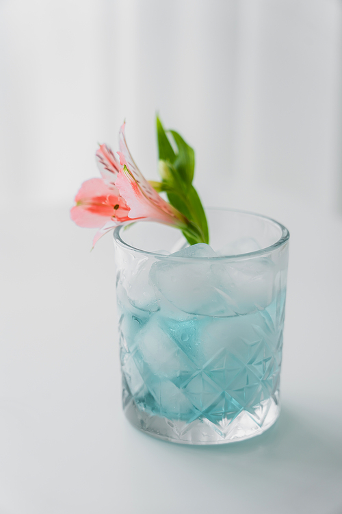 crystal glass with pink alstroemeria flower and iced tonic drink on white background