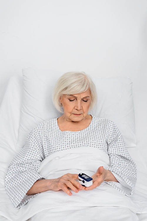 Senior patient using oximeter on bed in hospital ward