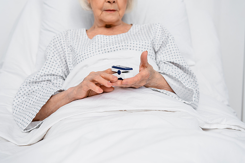 Cropped view of oximeter in hands of senior patient on hospital bed